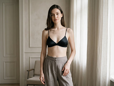 Woman wearing a black triangle bralette with gray trousers in a softly lit minimalist interior