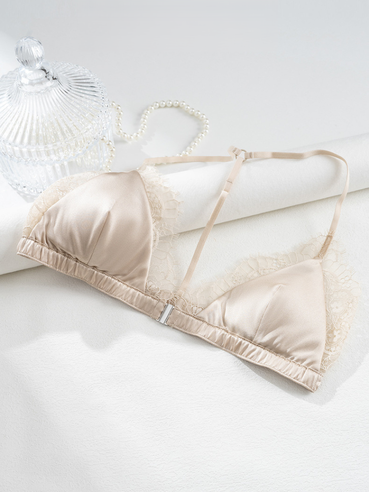 Champagne silk and lace triangle bra displayed on a white surface beside a glass jar and a strand of pearls.