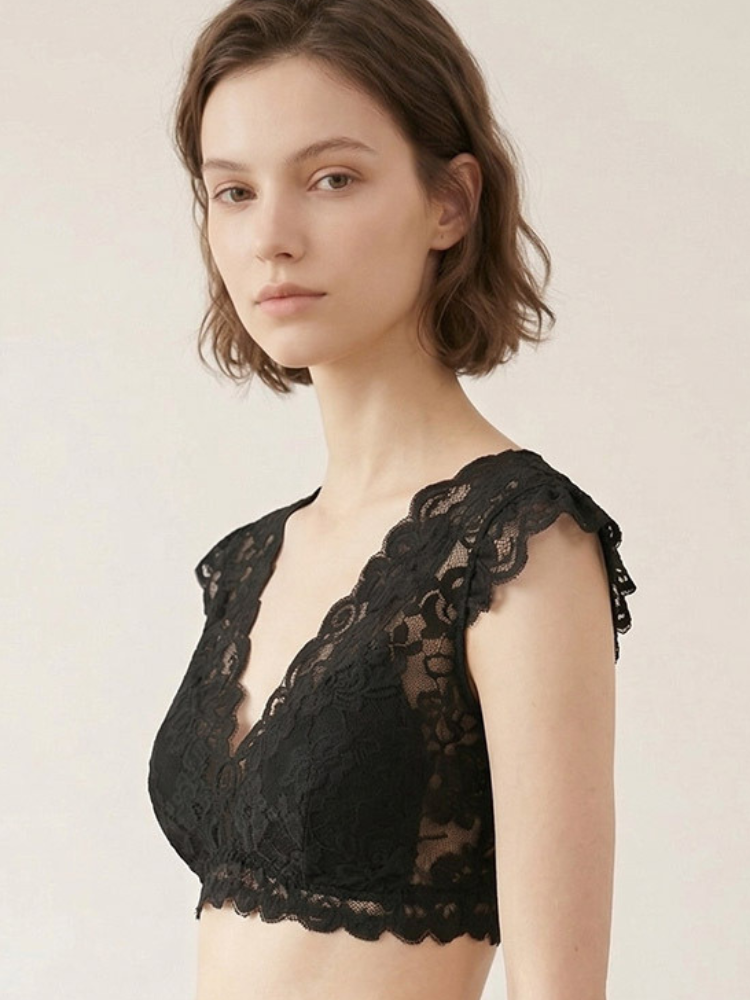Model wearing a black floral lace bralette with short lace cap sleeves, a deep V-neckline, and a scalloped underbust hem.