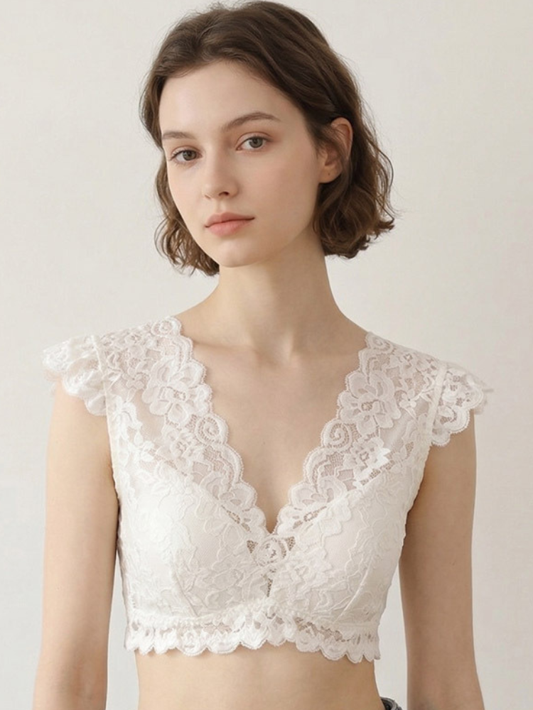 Model wearing a white floral lace bralette with delicate cap sleeves, a plunging V-neckline, and scalloped lace trim.