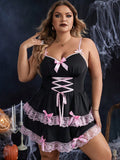 Plus size model wearing a black lace-up tiered chemise dress with pink bow accents and matching brief